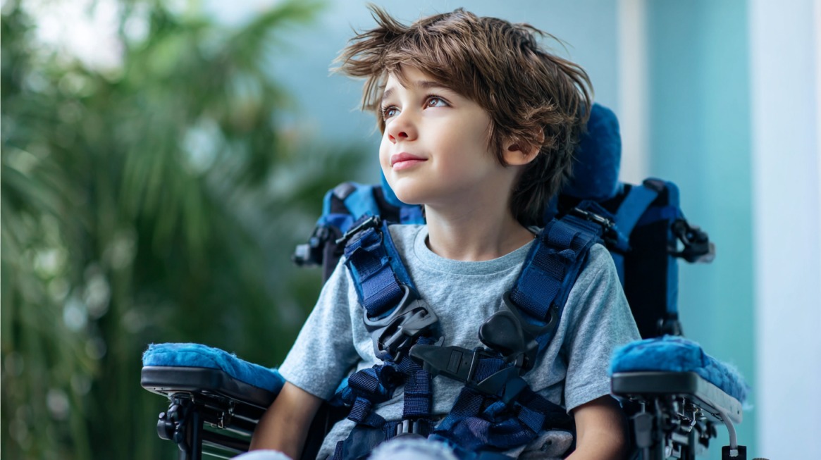 Young boy in a wheelchair with supportive straps, looking upward with a calm expression