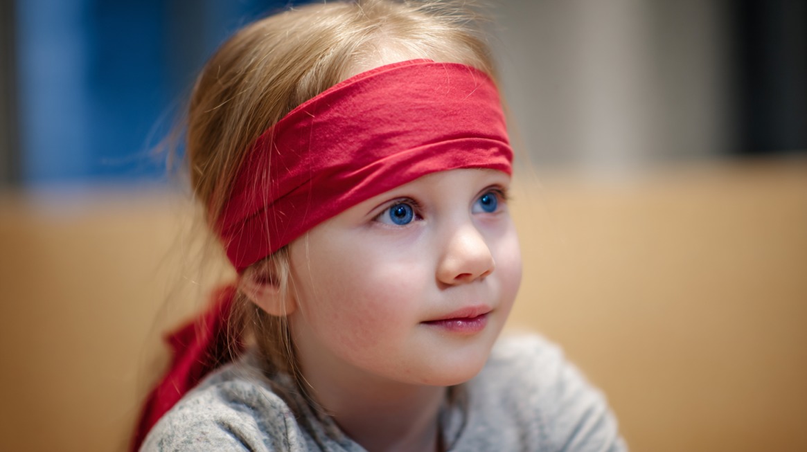 Young child wearing a red headband looking attentively to the side indoors