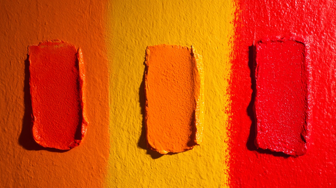 Three textured paint swatches in red orange and yellow on a colored background
