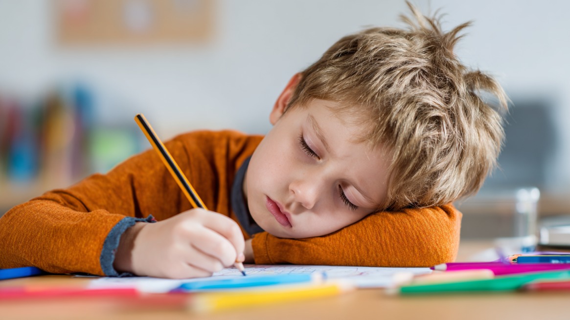 Young child leaning over a desk while writing with a pencil