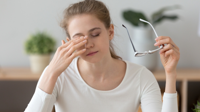 Woman rubbing her eyes and holding glasses due to visual fatigue