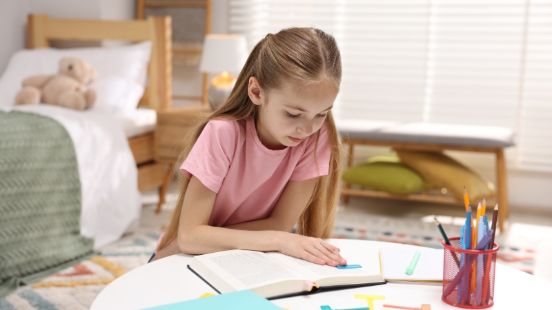 A young girl focuses on reading a book at her desk, showing the effort many dyslexic kids put into learning