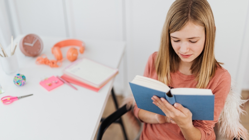 A teenage girl reads a book at her desk, representing supported dyslexic individuals building skills for future success