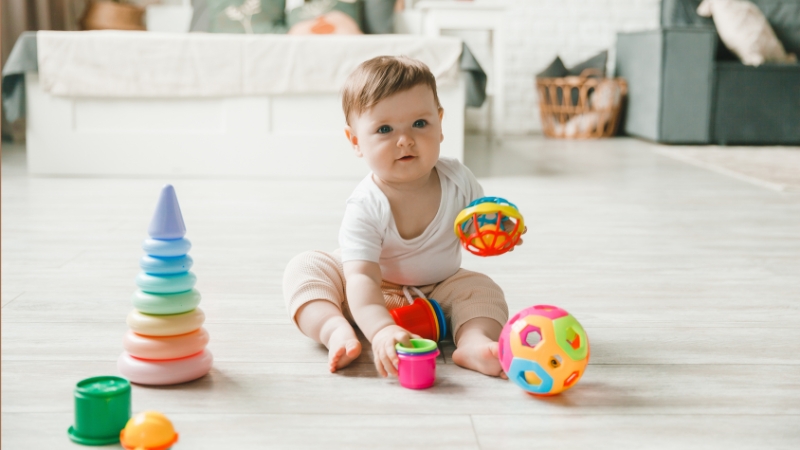 6-month-old baby sitting on the floor and reaching for toys while exploring objects