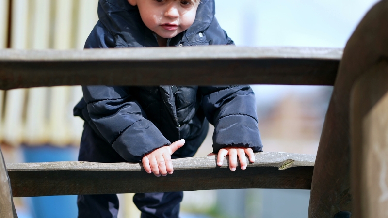 Toddler climbs on playground bars to build balance, strength, and coordination