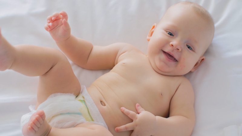 Baby moves arms and legs while lying on back and smiles during early motor development