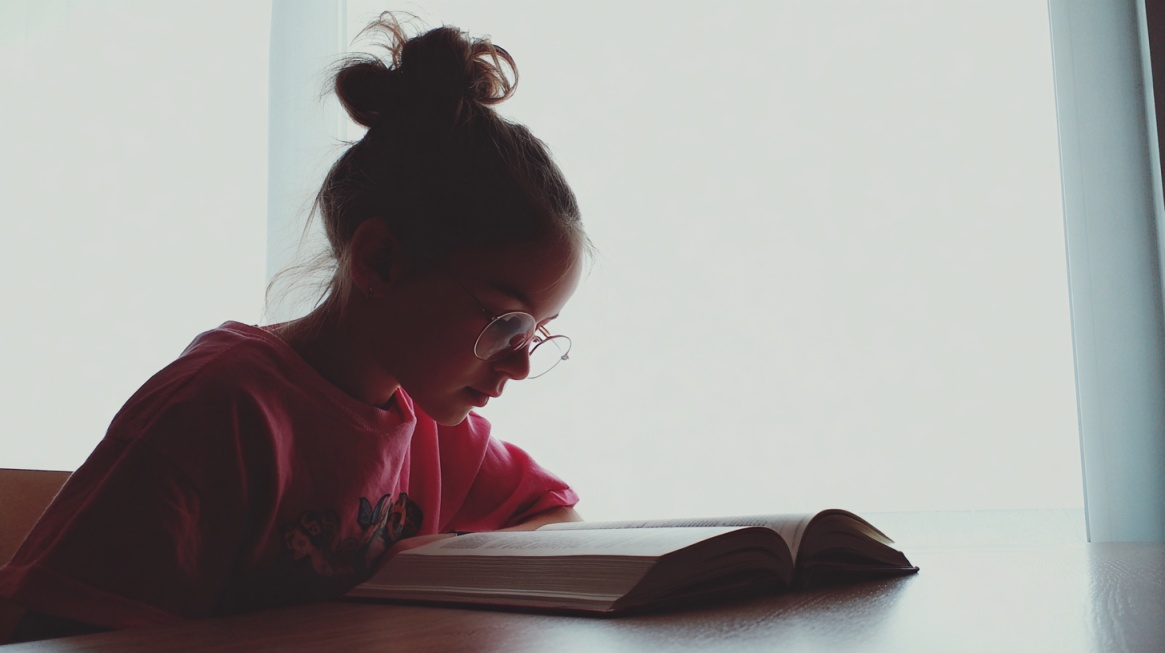 Student reading a book at a desk near a bright window