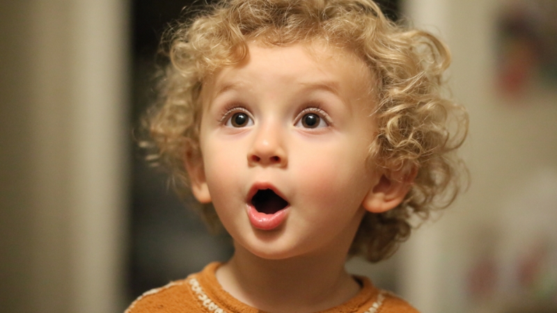 Toddler with curly hair and surprised expression during early speech stage