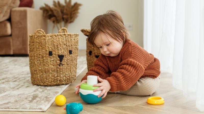 Baby uses hands to place a toy piece into a container on the floor