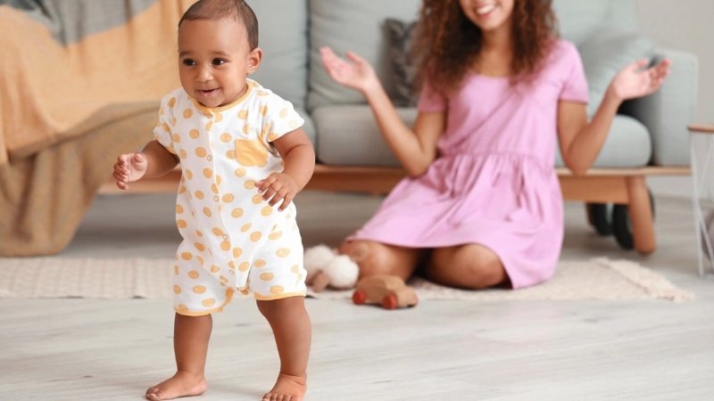 Baby takes first steps on the floor while a parent encourages nearby