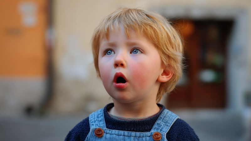 Three-year-old child speaks outdoors with mouth open