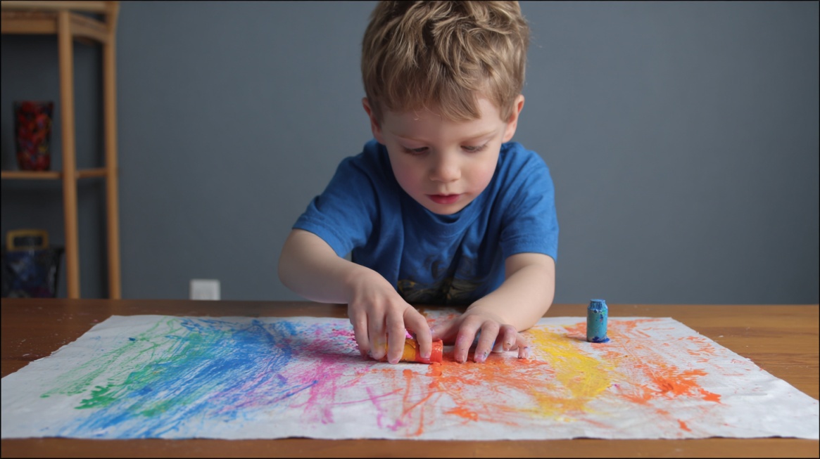 Young child using crayons to make colorful marks on paper while focusing on the activity.
