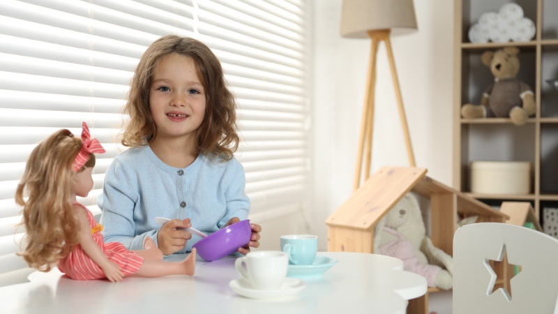 Toddler feeds a doll with toy dishes during pretend play to build imagination and social skills