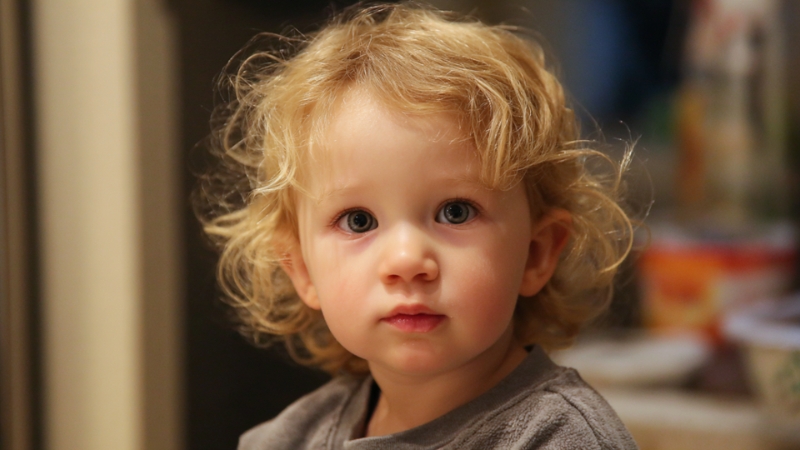 Toddler with curly hair looking directly at the camera indoors