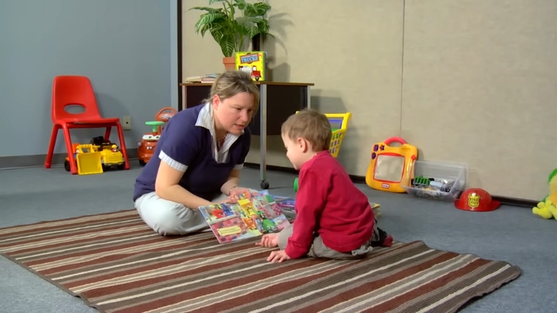 Adult and young child sit on the floor and look at a picture book together