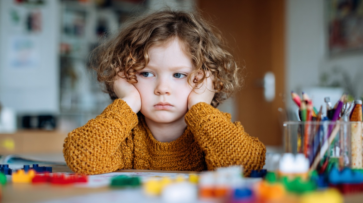 Young child sitting at a table with toys, appearing disengaged or withdrawn