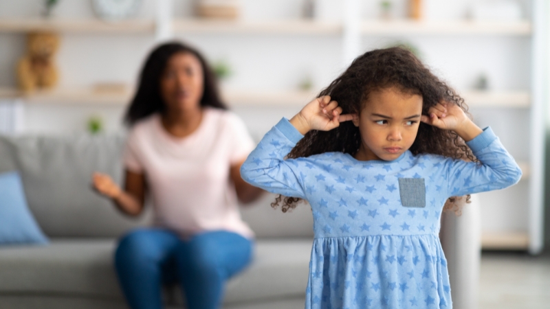 Child covering ears and looking upset while a parent speaks in the background