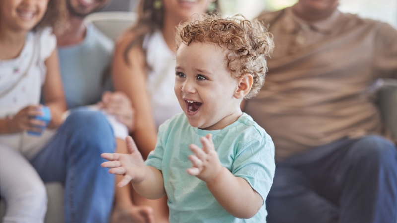 Baby smiles and claps while interacting with family during social development