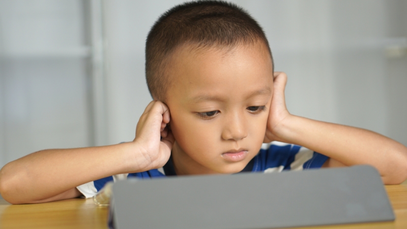 Child covering ears and looking overwhelmed while sitting in front of a screen