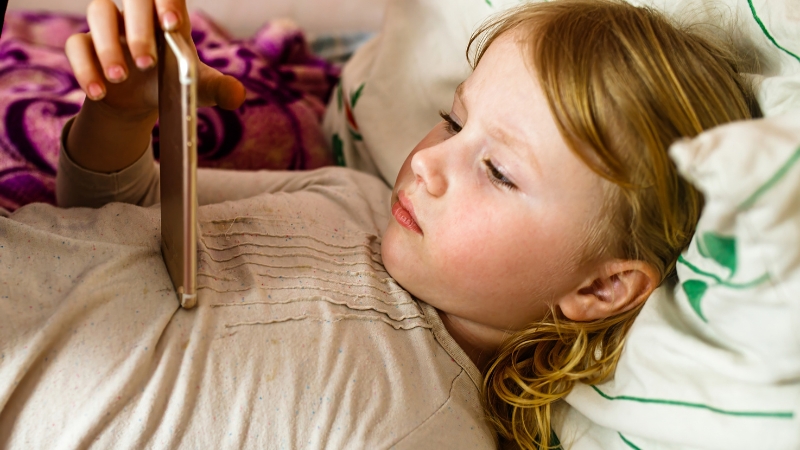 Toddler lies on a bed using a phone during quiet time instead of active play