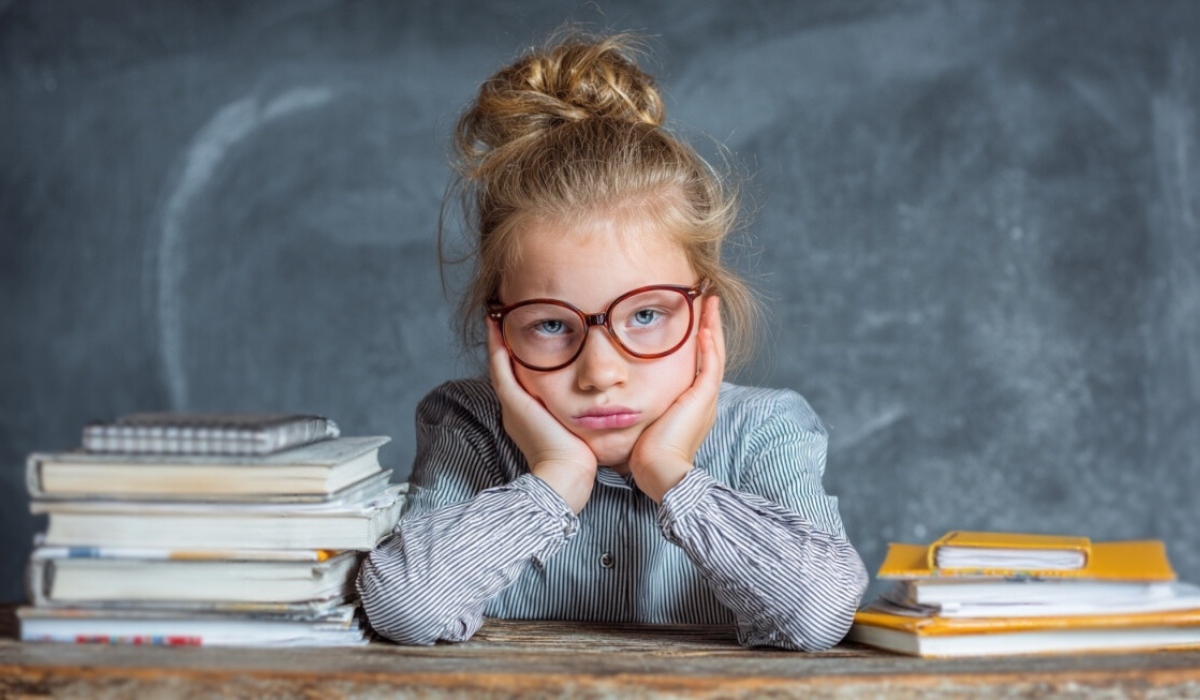 Student sitting at desk with books looking tired or bored