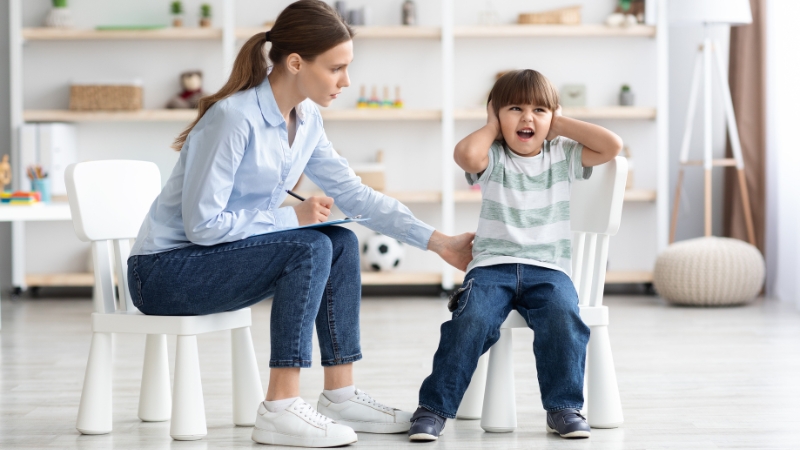 Child covering ears in distress while an adult offers support during sensory overload