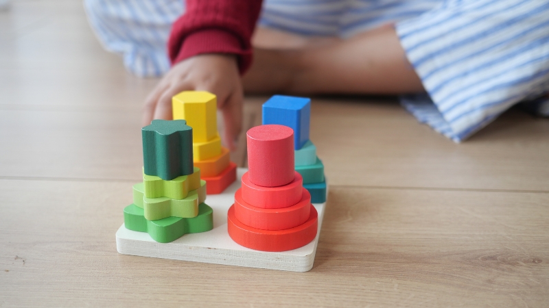 Toddler stacks colorful shape blocks on a wooden toy to build coordination and problem solving skills