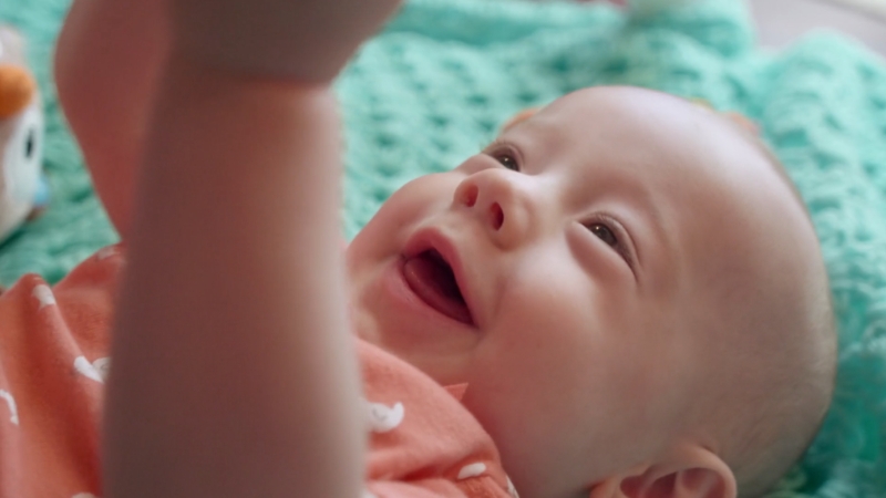 Baby smiles and looks at caregiver during early social interaction on a play mat
